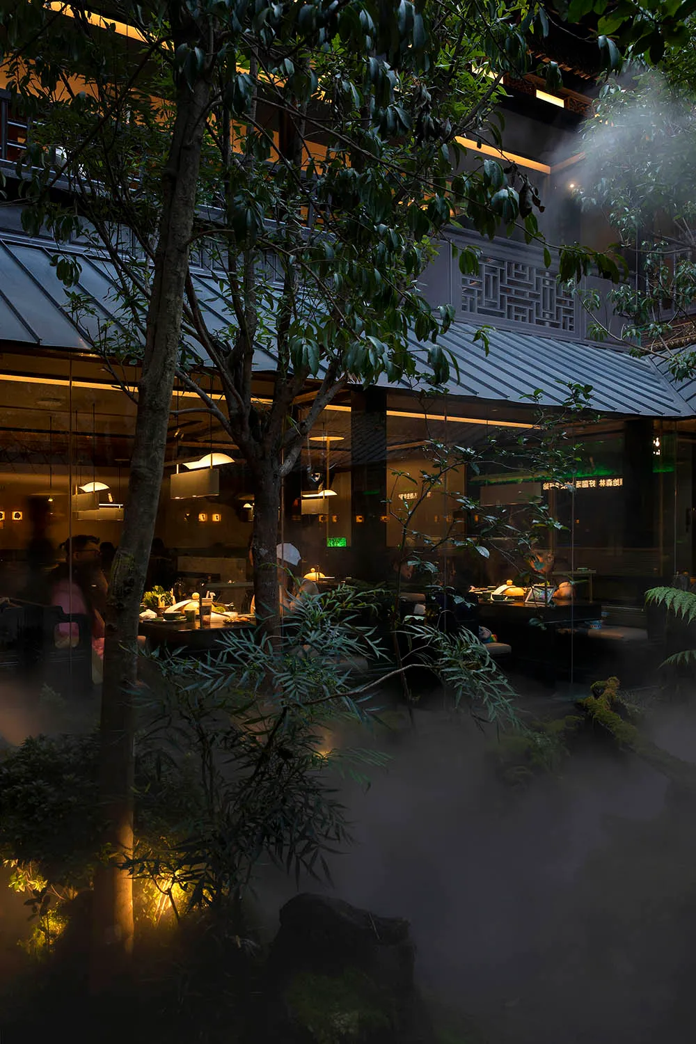 Outdoor view of an industrial-themed restaurant with metallic accents, glass walls, and a concrete structure.