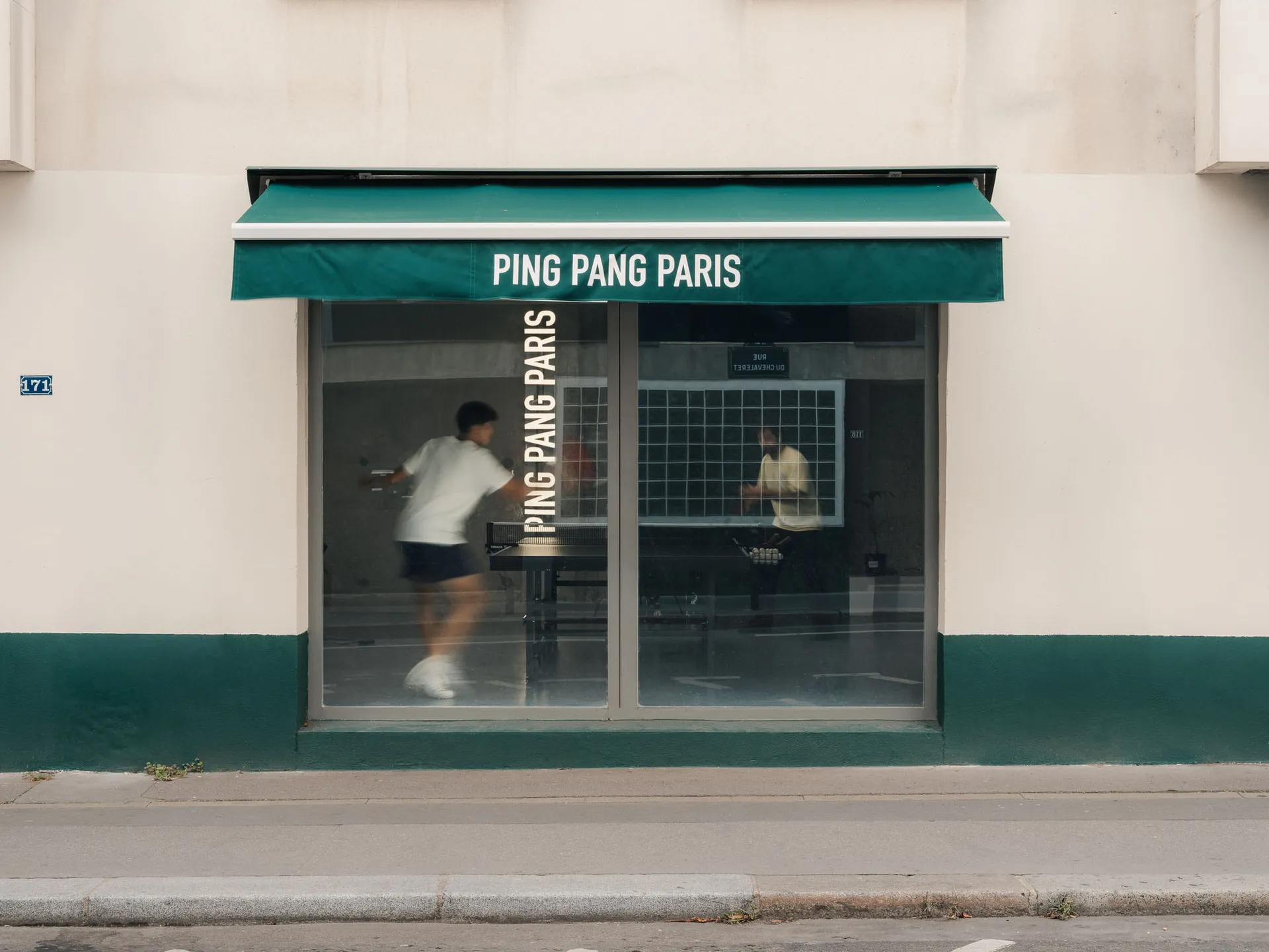A storefront window displaying a table tennis game with people playing inside.