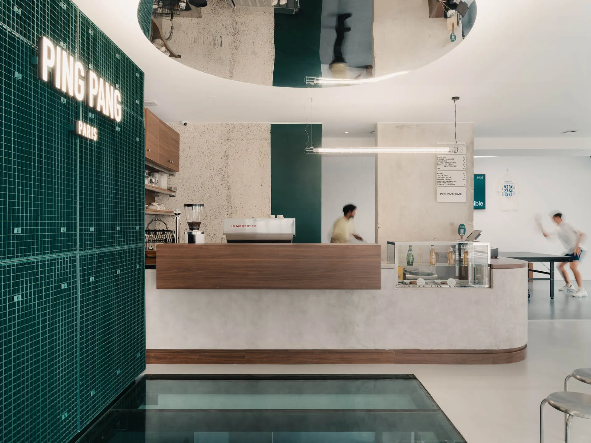 A modern cafe interior with a concrete and tile counter, featuring a coffee machine and a man working behind it.