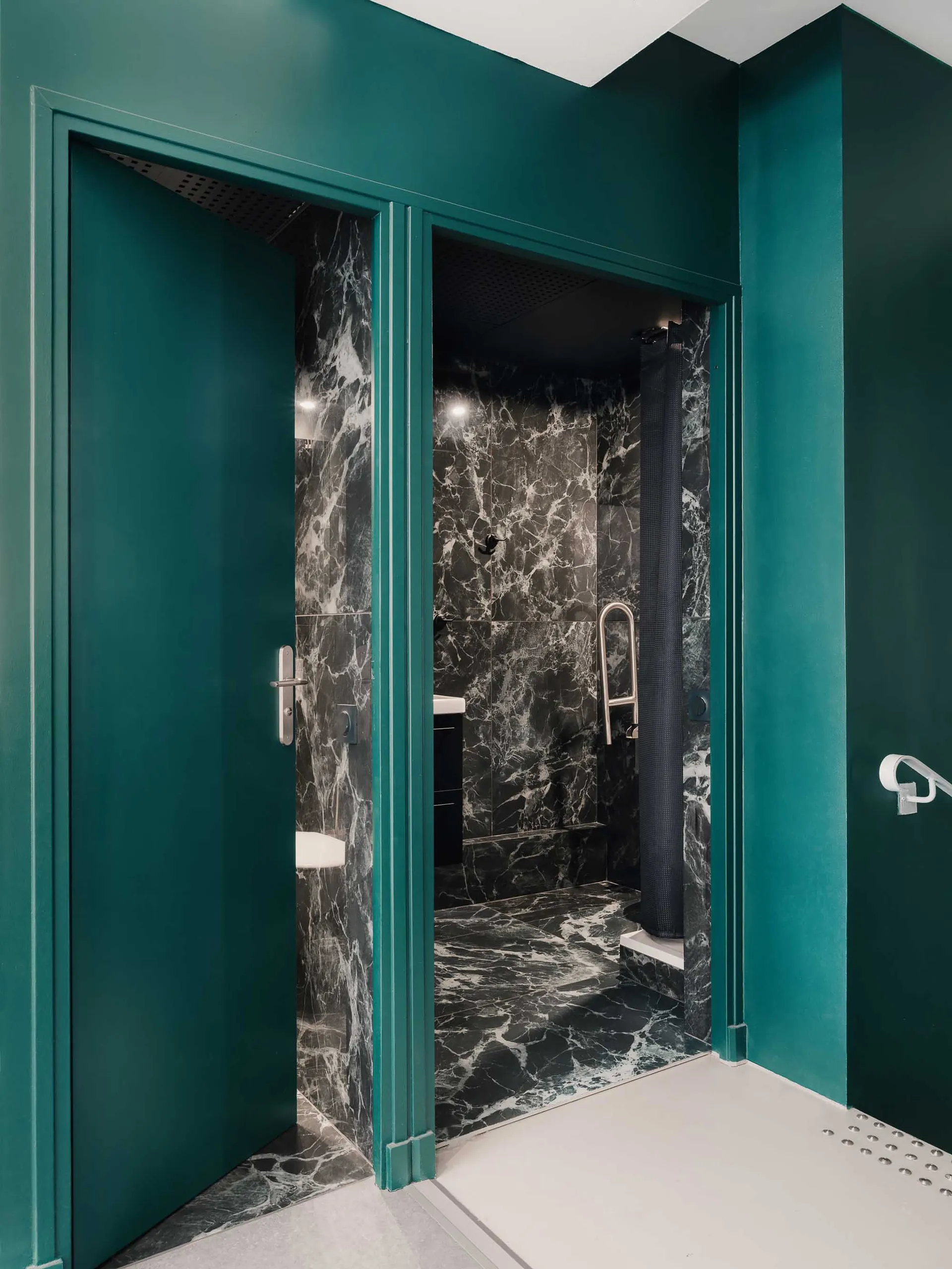 A modern bathroom with marble tiles and green walls and door frames.
