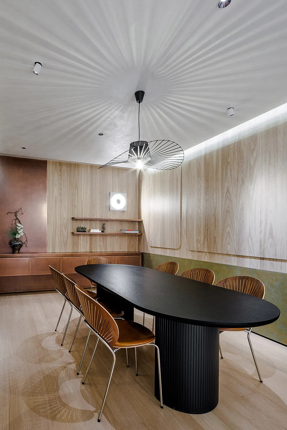 A modern dining room with wooden furniture, featuring a black dining table and chairs, a minimalist ceiling light fixture, an