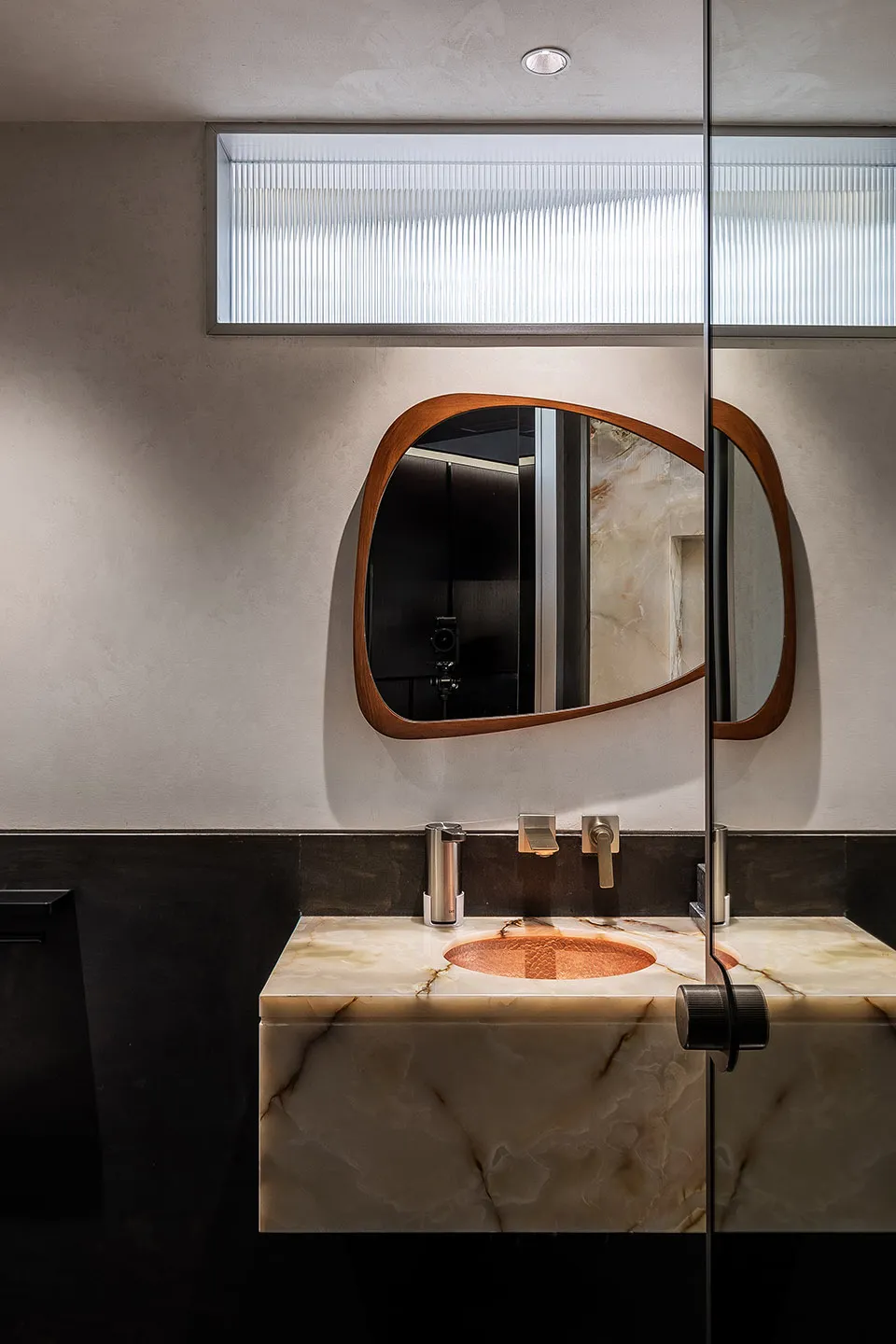 Modern bathroom with a marble sink and circular wooden-framed mirror.