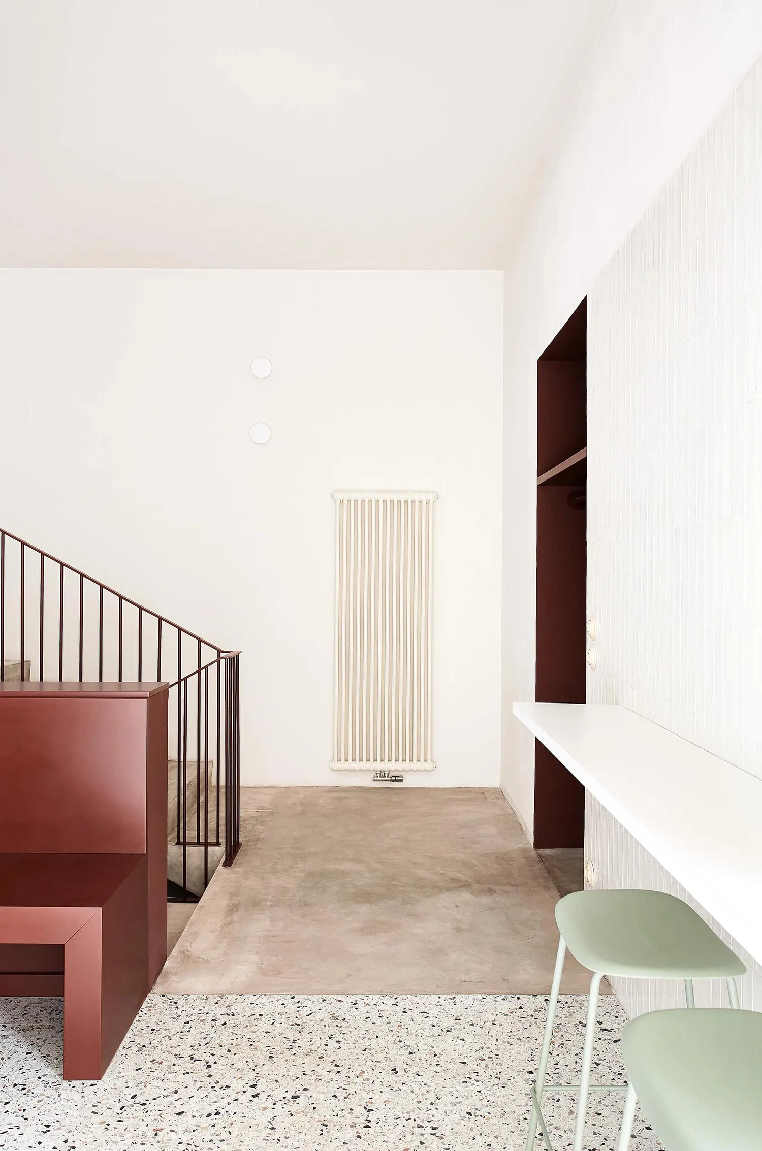 A minimalist interior with a concrete floor, white walls, and a simple red staircase.