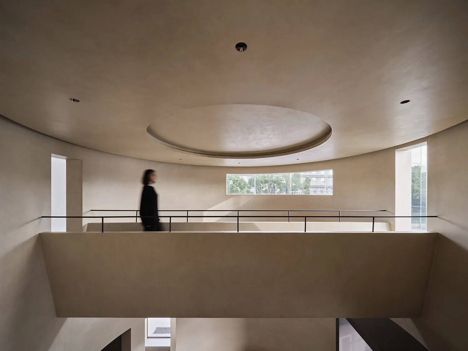 Modern architectural space with curved sandstone walls and a circular skylight.