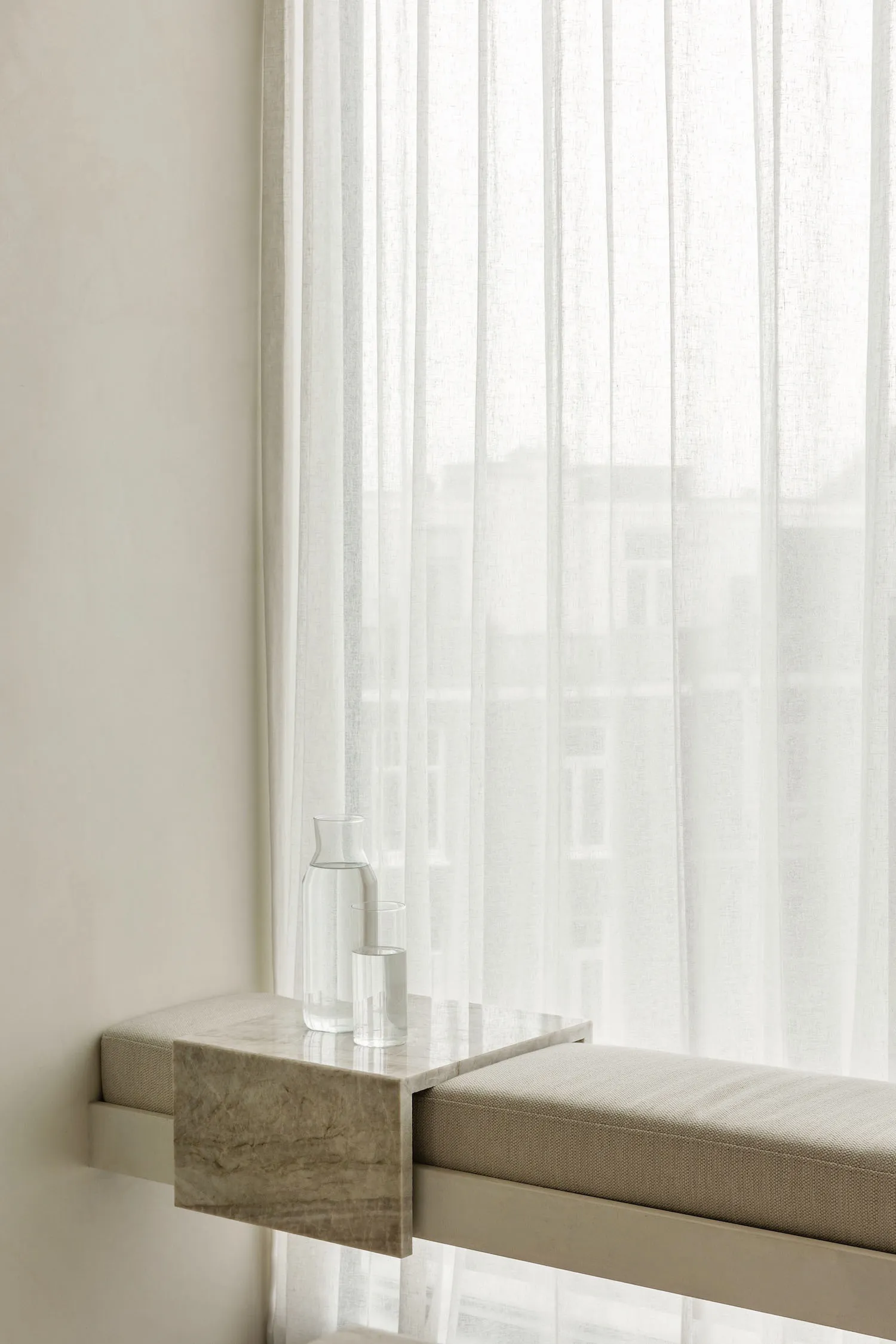 A modern window sill adorned with a marble table that holds a carafe and a glass of water.
