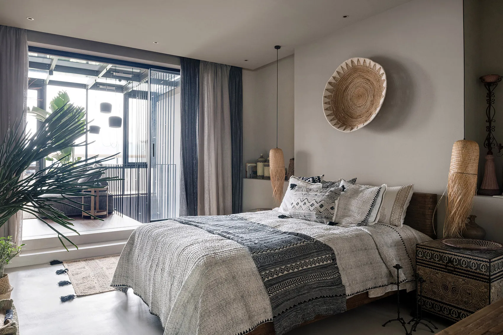 A boho-style bedroom featuring a bed with a woven headboard and decorative textiles, alongside ceramic and woven elements.