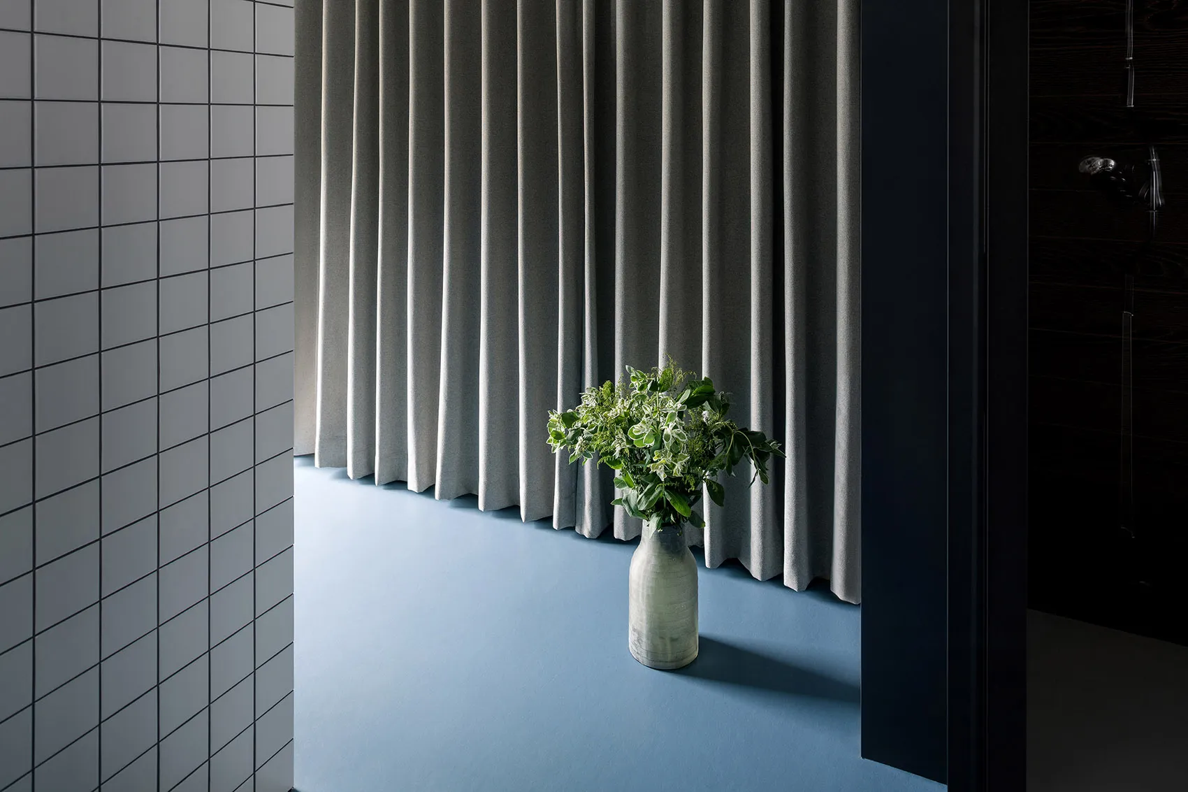 A minimalist interior featuring a gray curtain, vase with greenery, and minimalist decor.