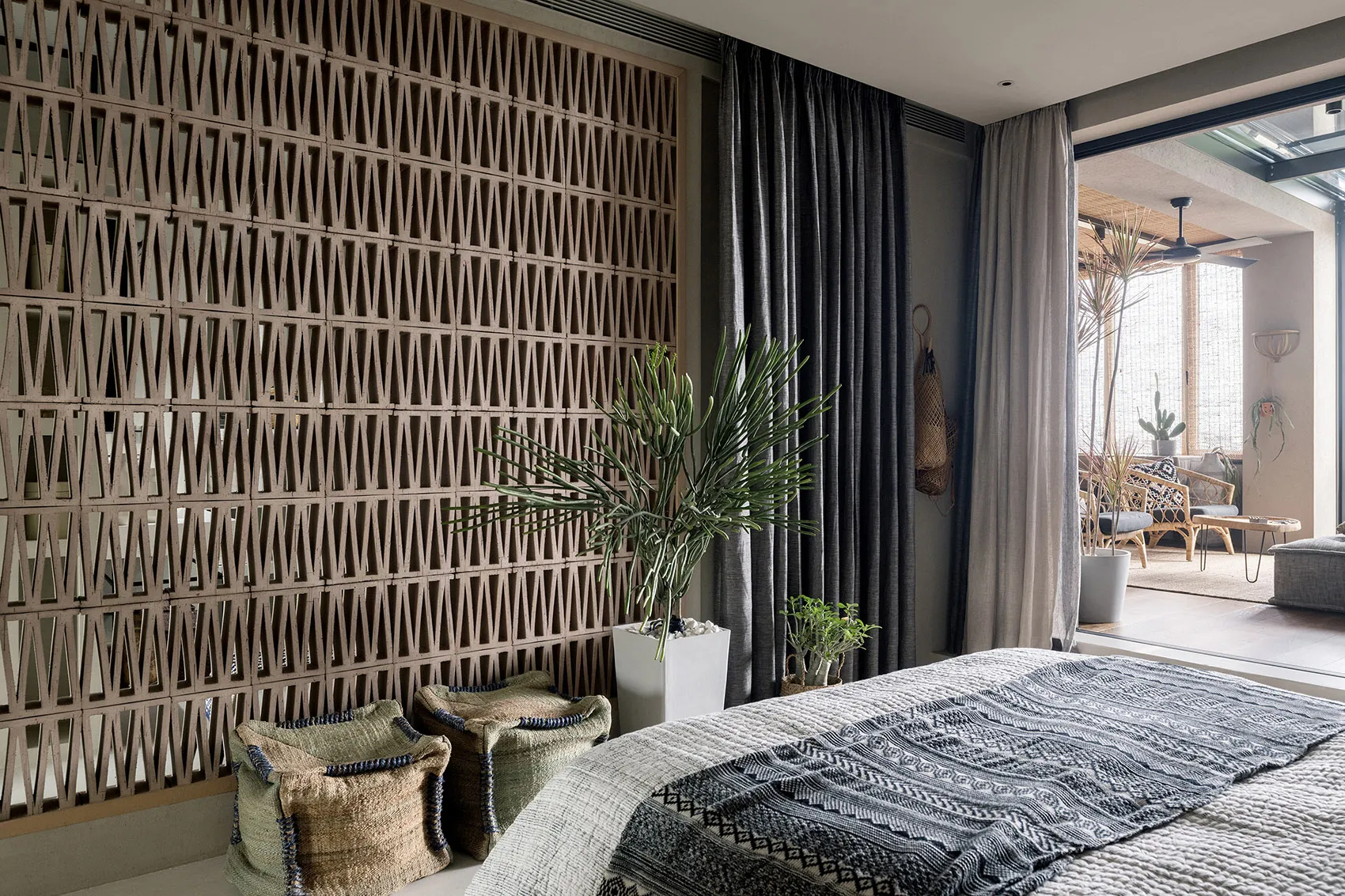A modern bedroom featuring natural fiber textiles, a geometric brick wall, and a large window with plants.