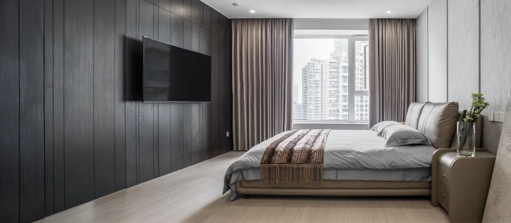 Modern minimalist bedroom featuring textured wood walls, a suede headboard, and a glass window with cityscape view.