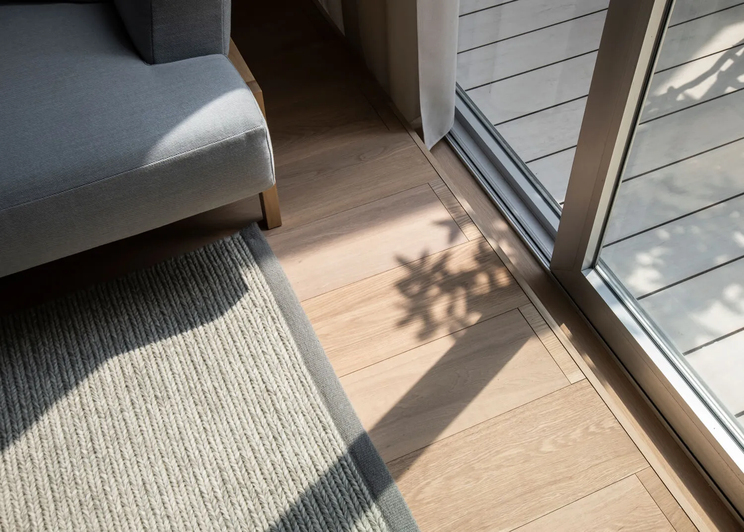A modern living room featuring wooden flooring, a gray fabric sofa, and a textured gray rug.