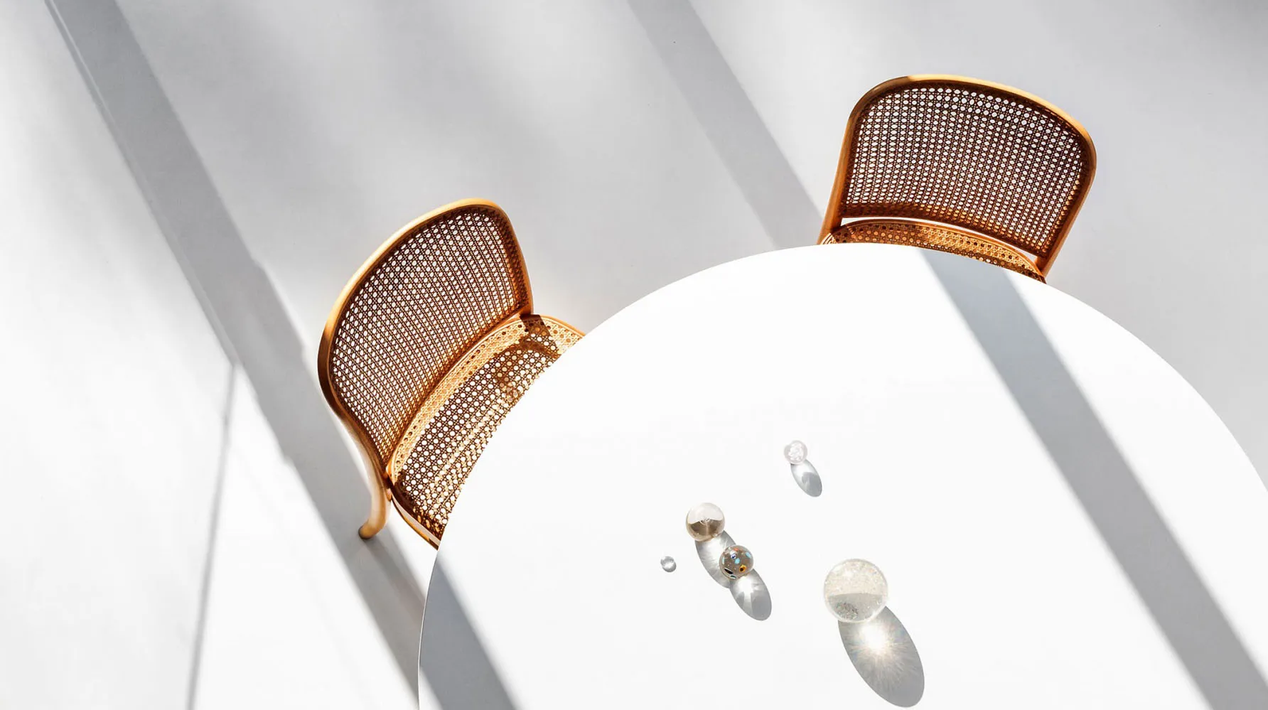 Two minimalist metal-woven fabric dining chairs with a white round table.