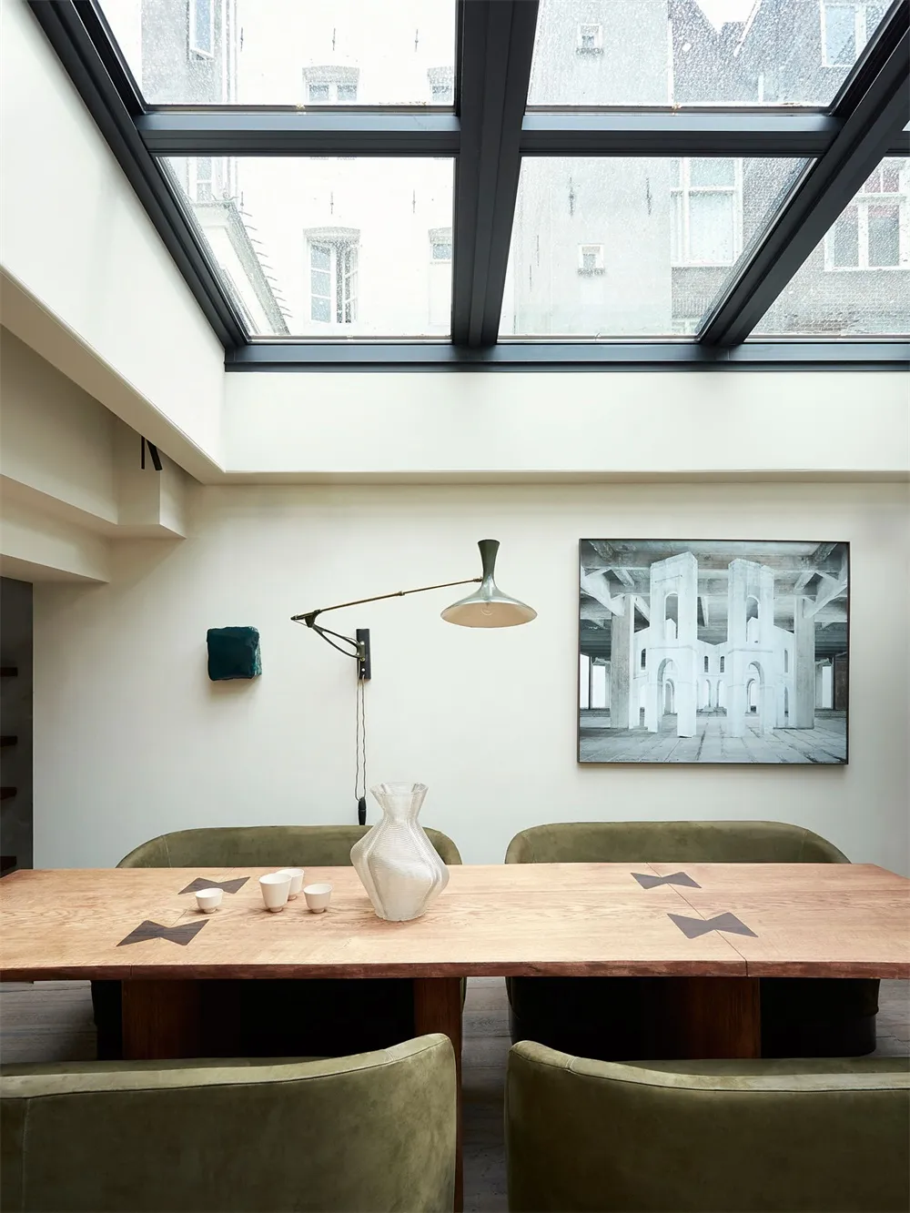 Modern dining room with wooden table and chairs, featuring a large window with city view and abstract painting on the wall.