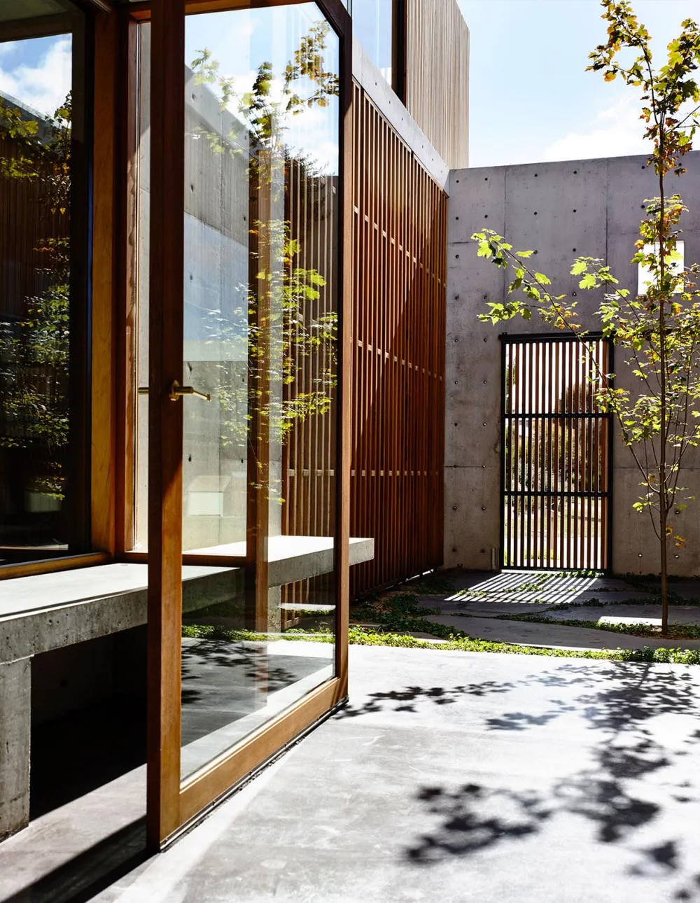 A modern front door made of concrete, glass, and wood, featuring a glass panel and wooden slats.