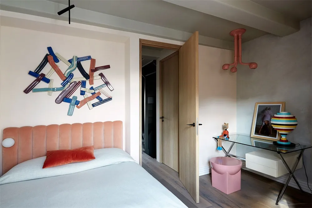 A minimalist bedroom with a pink bed, white bedding, and a colorful abstract sculpture on the wall.