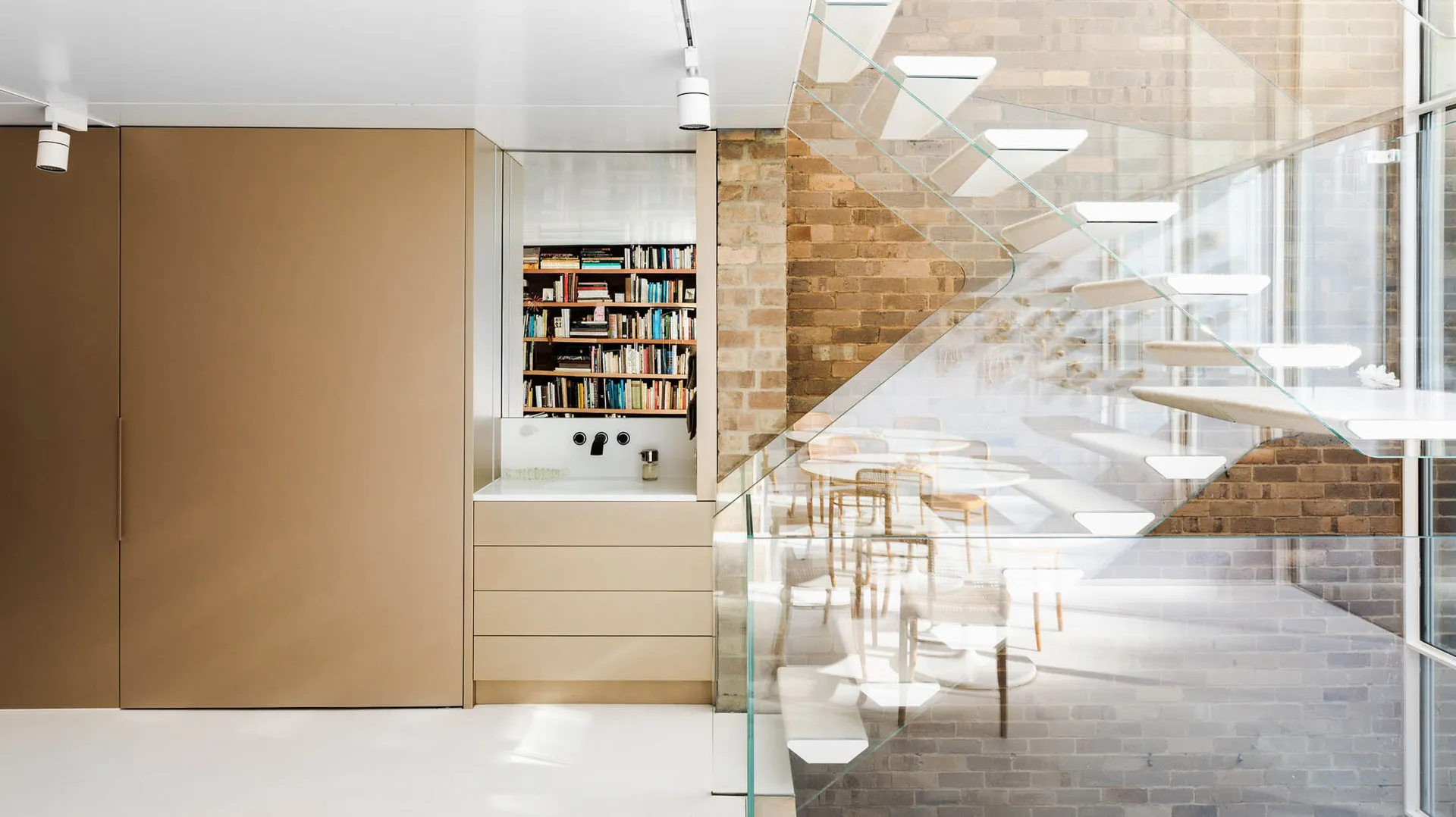 A sleek, modern office space featuring glass, metal, and concrete materials, with a glass-enclosed staircase and bookshelves.