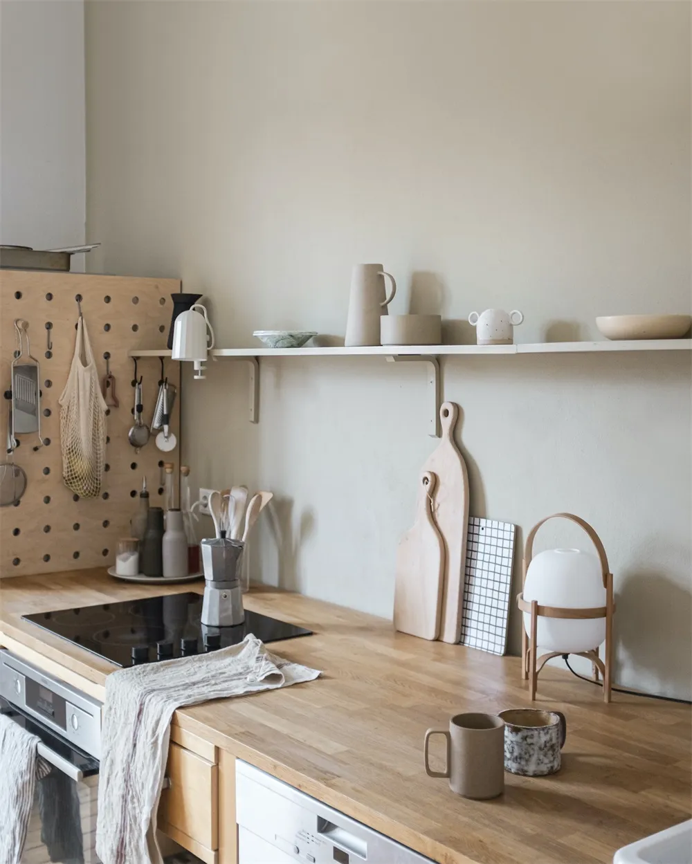 A minimalist kitchen with a wooden countertop, hanging utensils, and various mugs and bowls on a shelf.