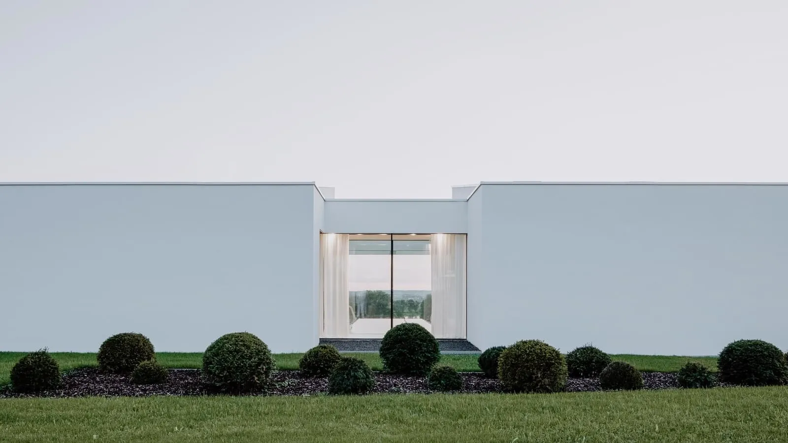 Modern residential exterior with minimalist design featuring white stucco walls and large glass window.