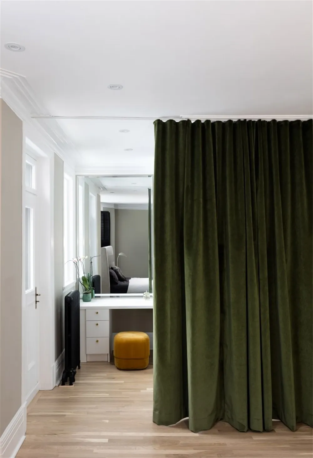 Modern bedroom with green velvet curtain, white walls, hardwood floor, and black radiator.