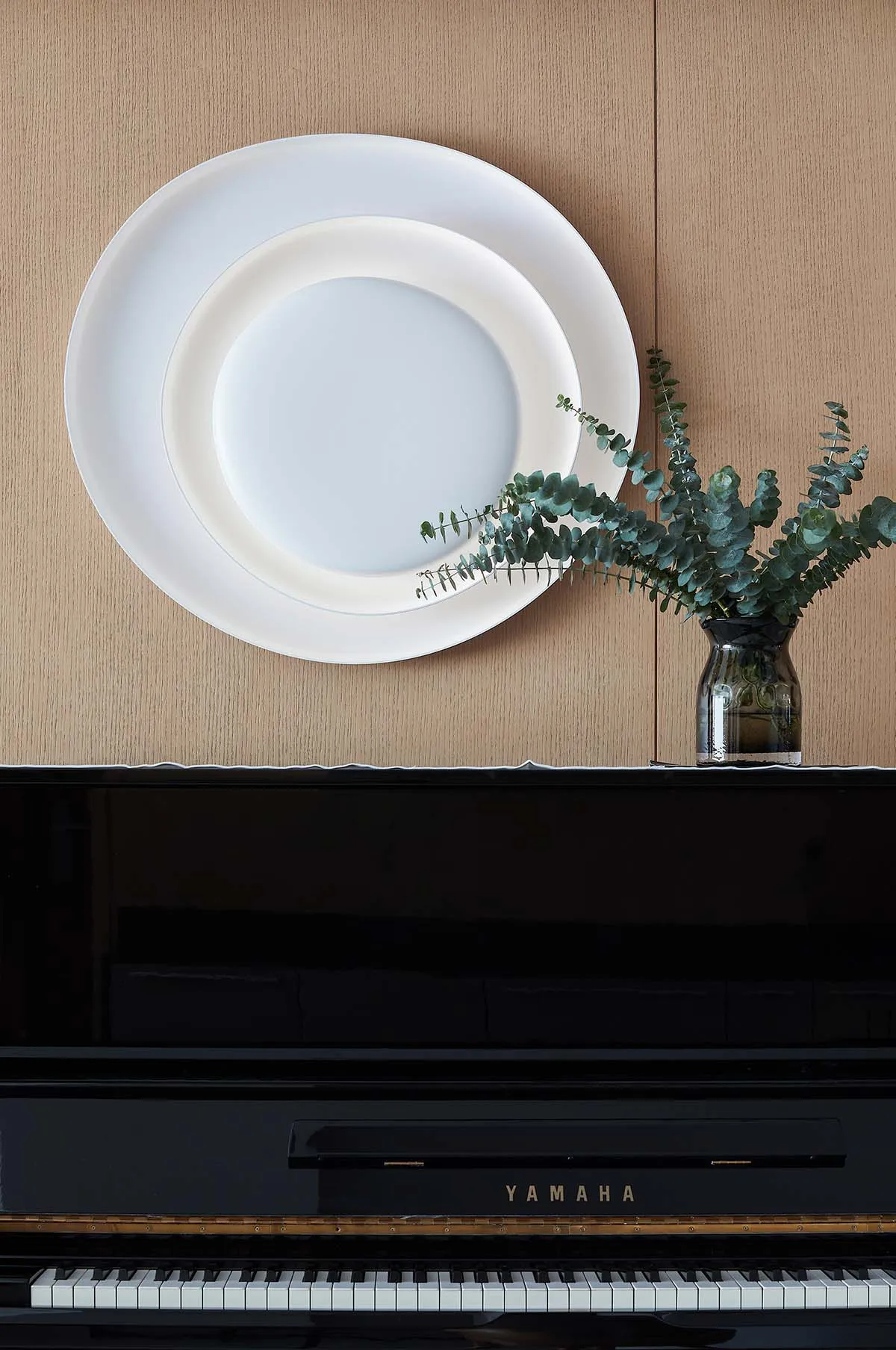 Ceramic plates arranged on the wall with greenery in a vase on top of a black Yamaha piano.