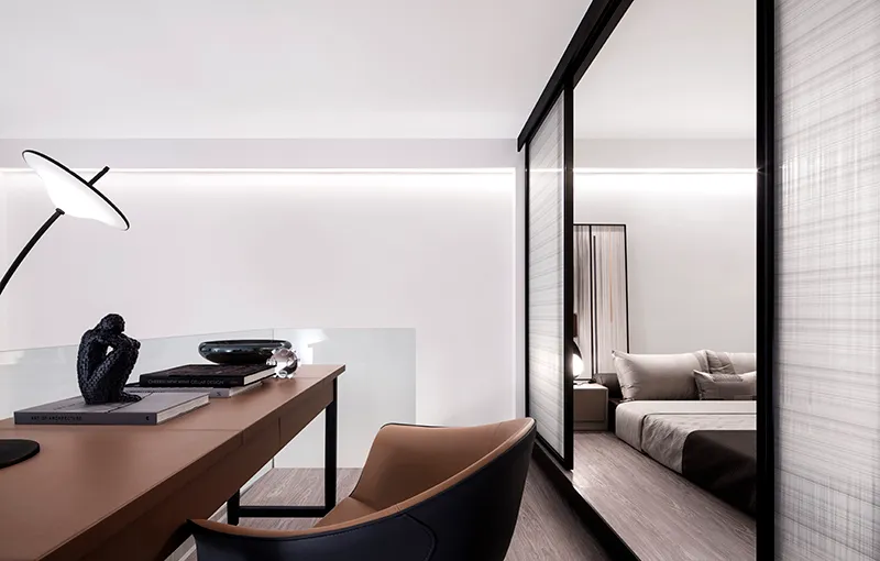 A modern minimalist bedroom featuring transparent glass walls and a sleek desk.