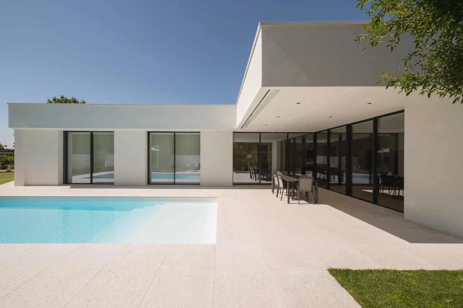 Modern minimalist home with white walls, large glass walls, and an outdoor pool under a clear blue sky.