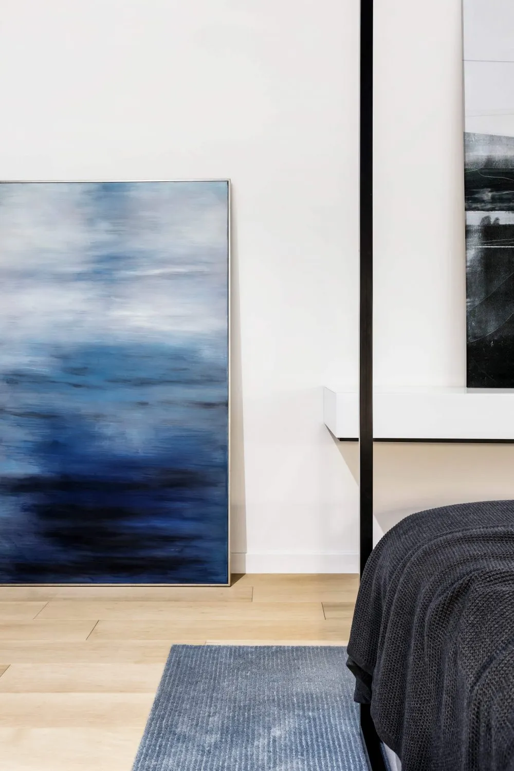 A minimalist interior design featuring a large abstract blue painting on a wall.