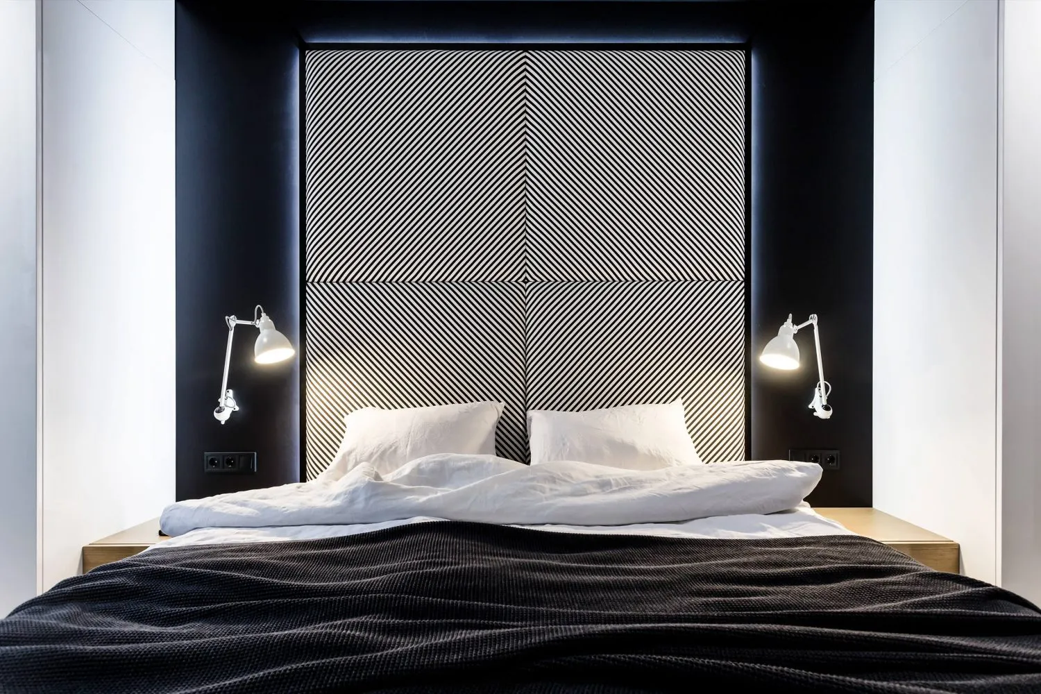 A modern minimalist bedroom with a textured fabric headboard and nightstands with white lamps.
