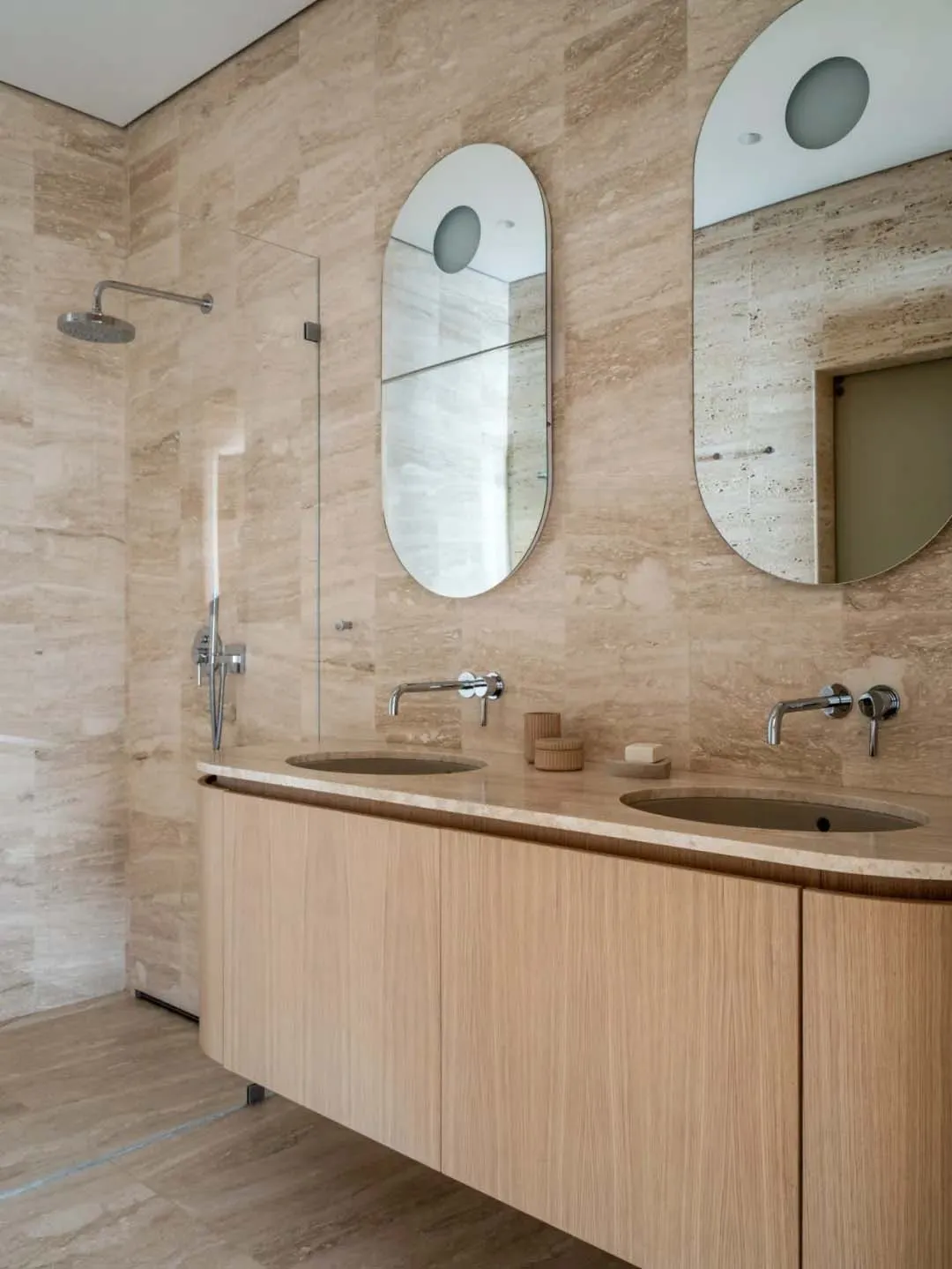 A modern bathroom featuring a wooden vanity with two sinks, a walk-in shower, and a mosaic tile floor.