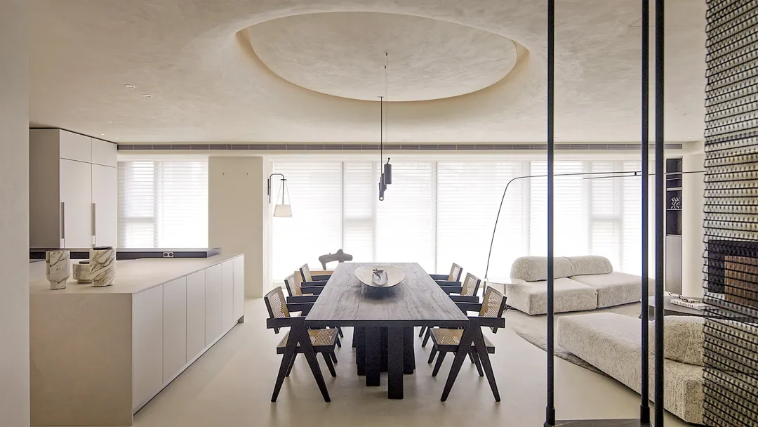 A modern dining room featuring a large marble dining table surrounded by black chairs, set against a minimalist backdrop with