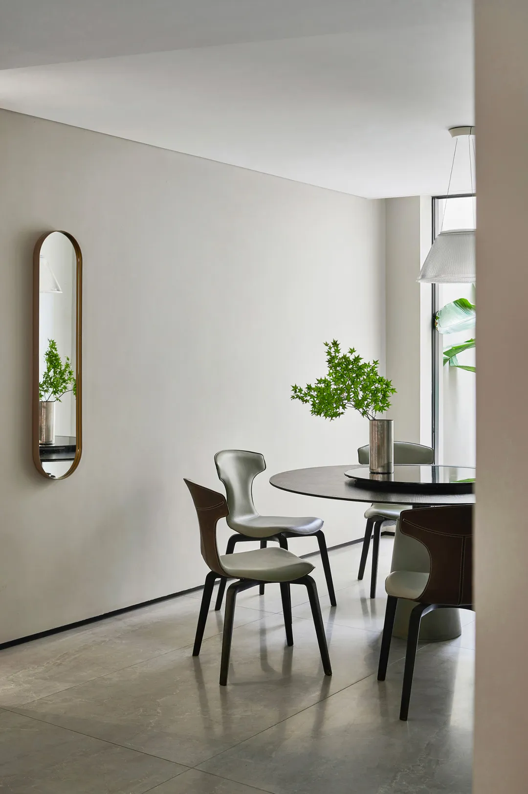 A modern, minimalist dining area with a round table, metal chairs, and a metal mirror.