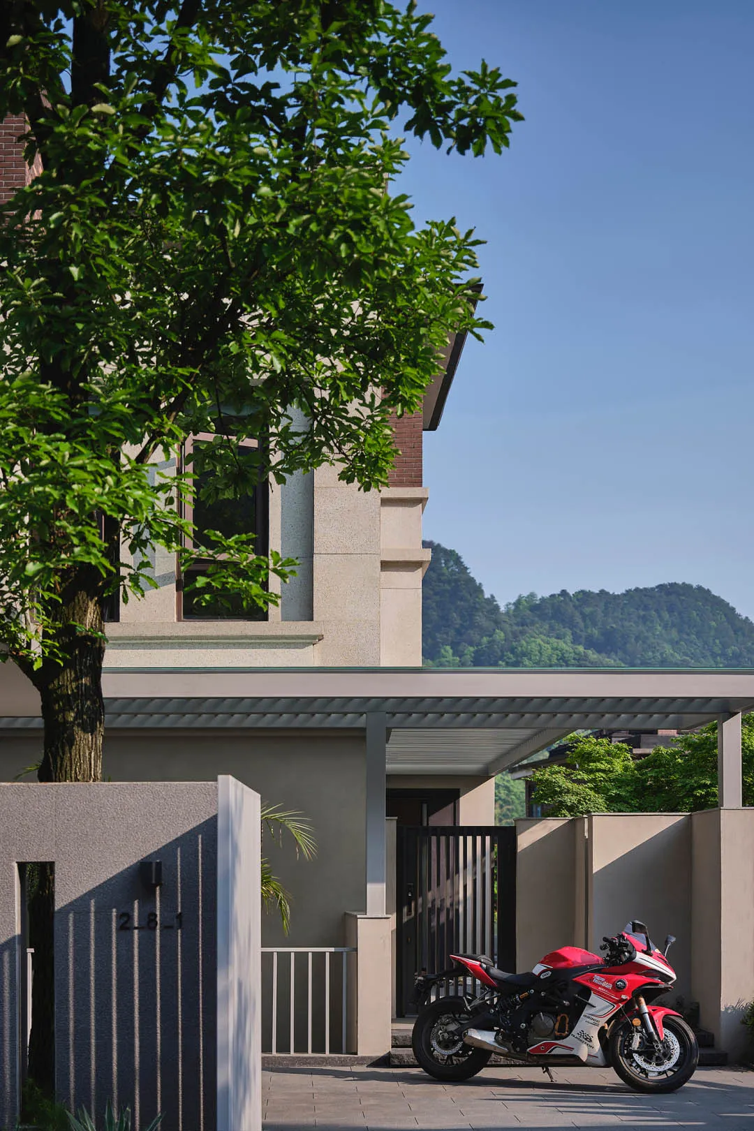 A modern residential exterior with concrete walls and a lush tree nearby.