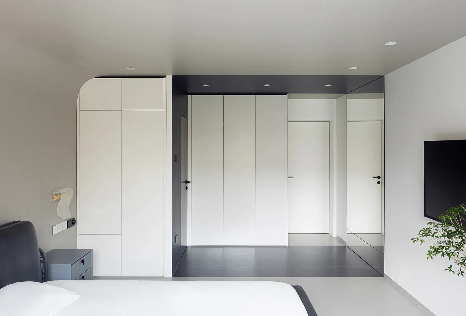A modern minimalist bedroom with white walls, a black headboard bed, and a minimalistic design.