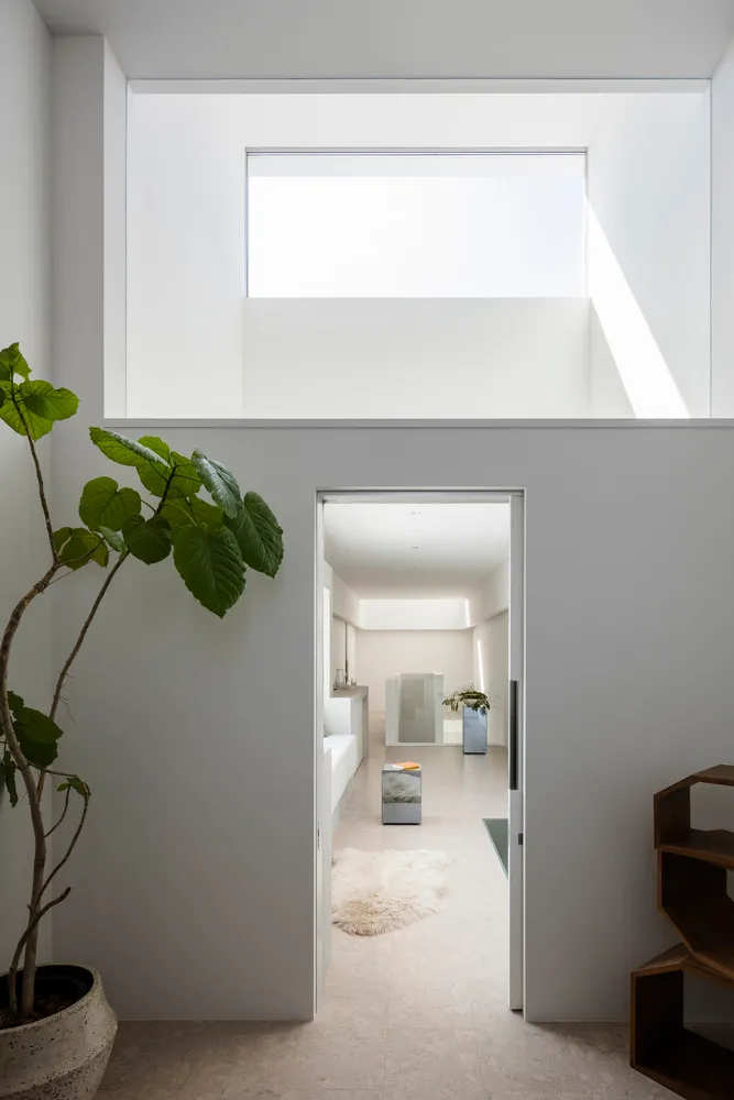 Modern minimalist living room with concrete walls and floor, large window, and plant.