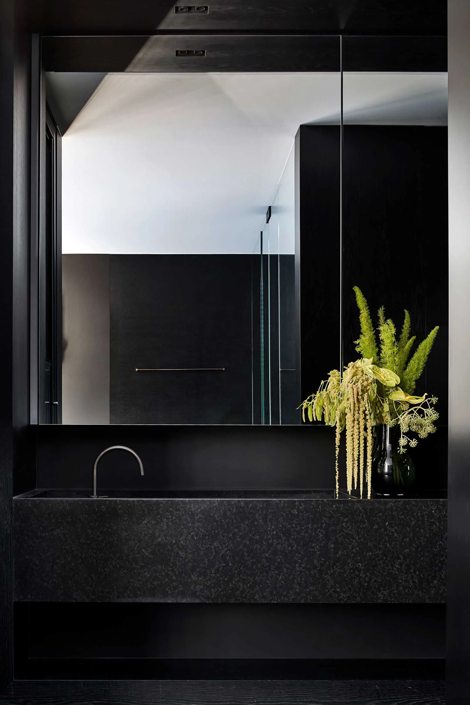 A modern bathroom with black granite countertops, a large mirror, and a vase of flowers.