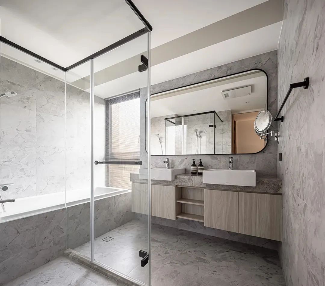 Modern minimalist bathroom featuring marble walls and floor, glass shower enclosure, and double sink vanity.