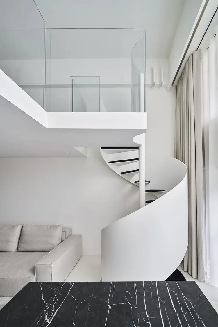 A modern residential interior featuring a spiral staircase with glass railings and white walls.
