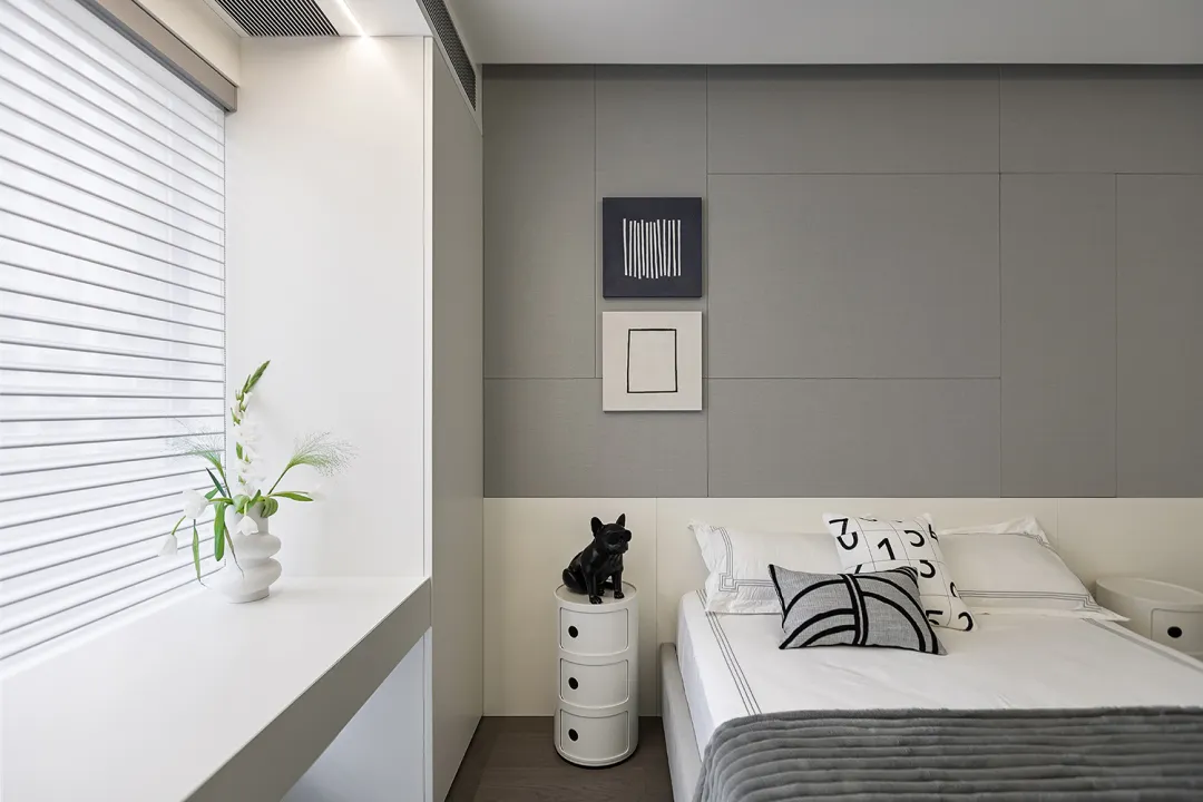 A minimalist bedroom with a grey and taupe color scheme, featuring a bed with white sheets and black and white pillows, a whi