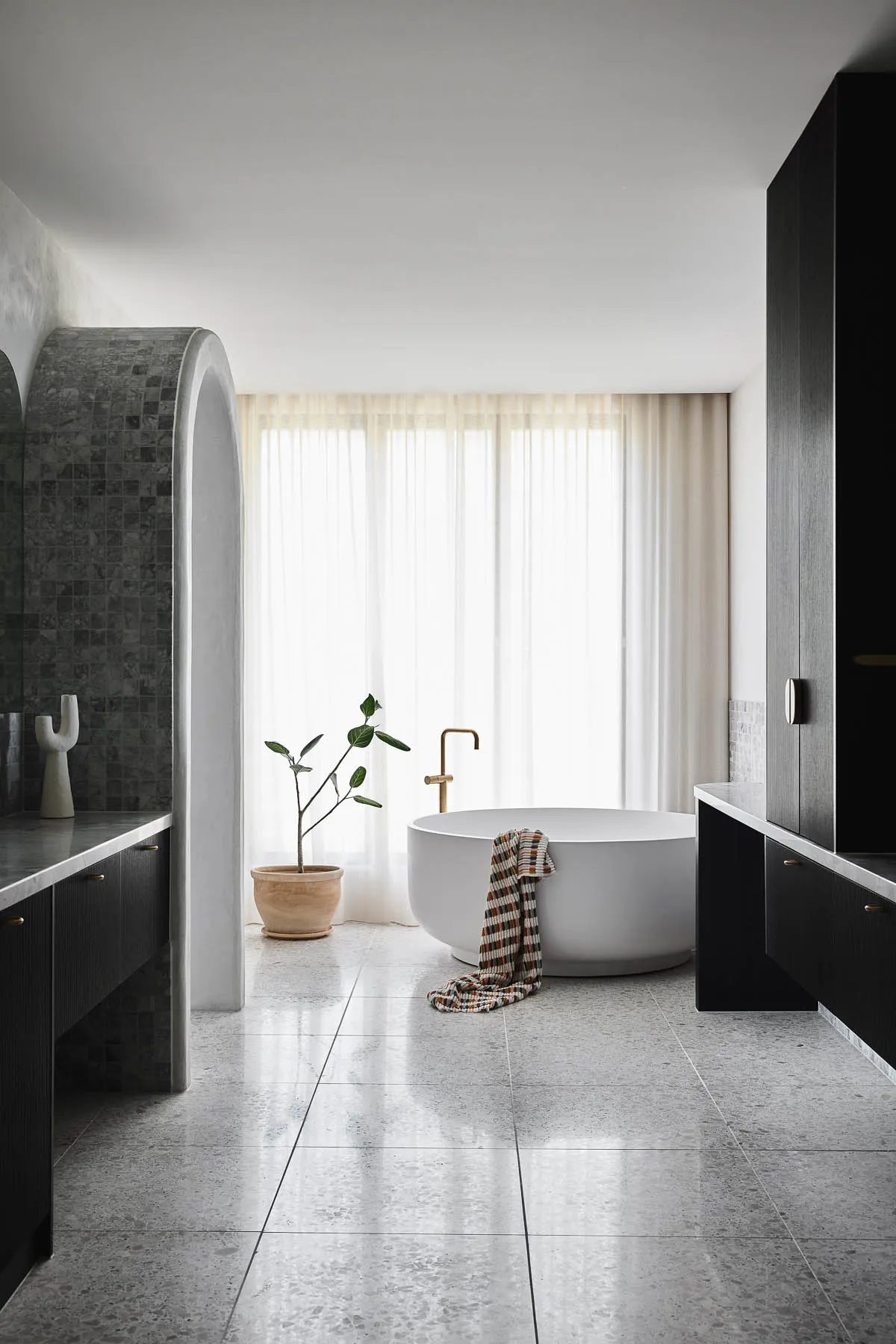 Modern, minimalist bathroom featuring a cement floor, white bathtub, natural light, and a single plant.