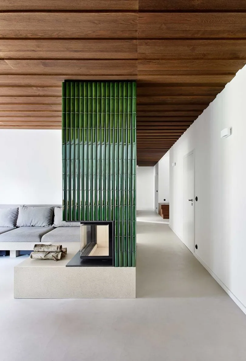 A modern living room with a green-tiled wall, concrete flooring, and a wood-paneled ceiling.