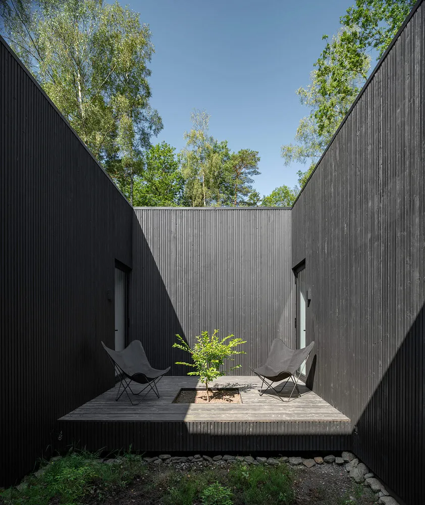A modern exterior with black wooden walls and a small courtyard with a tree and seating area.