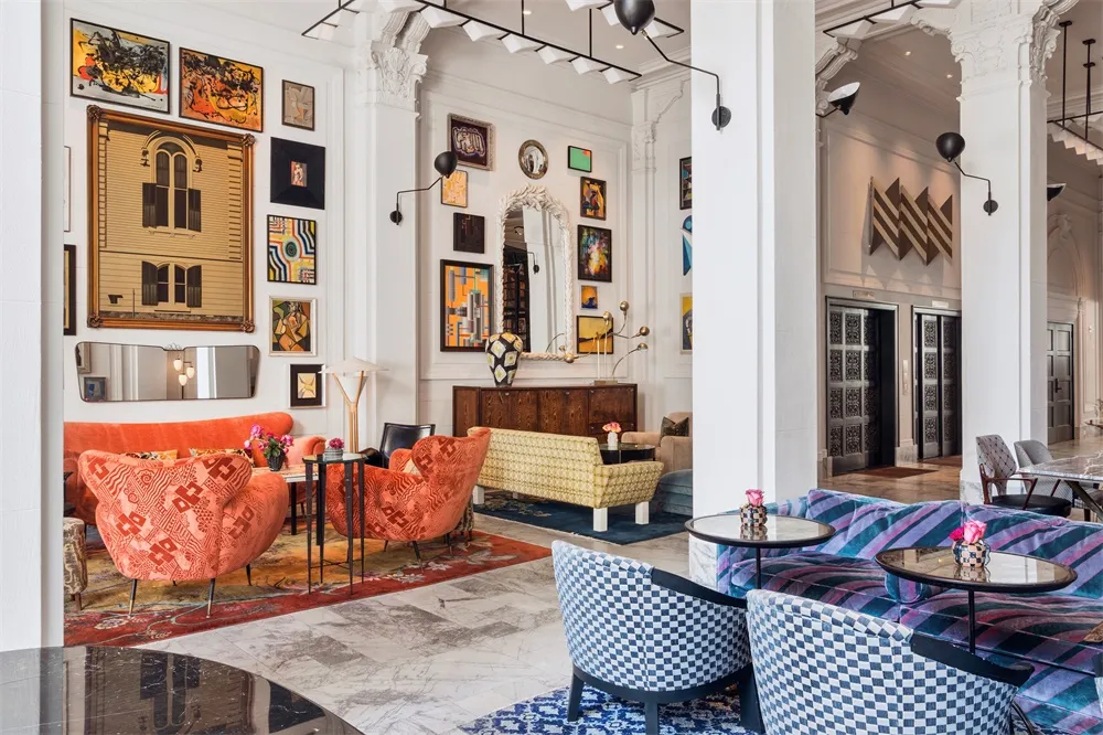 A vibrant, modern hotel lobby featuring concrete walls, patterned furniture, and a variety of art installations.