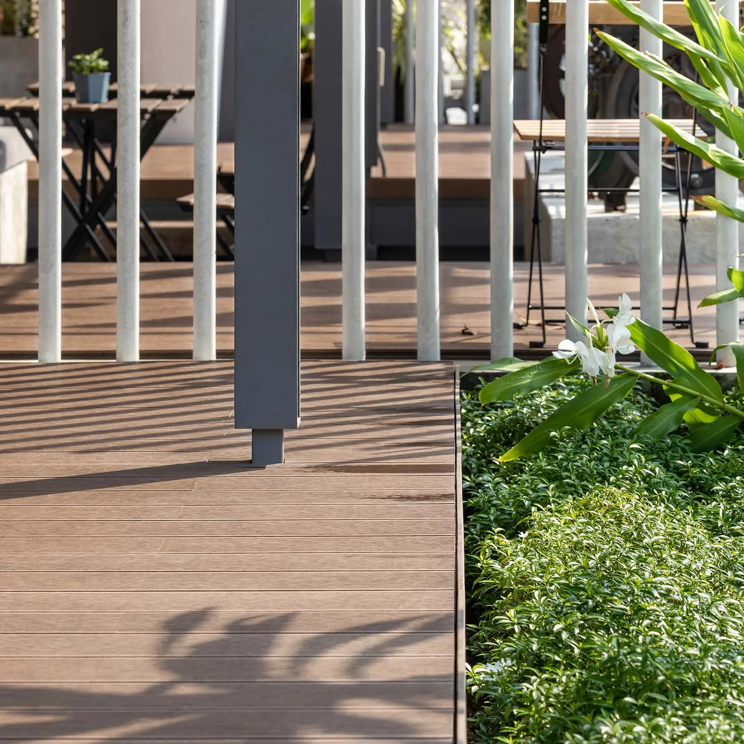 A wooden deck with metal railing, potted plants, and two chairs in a serene outdoor setting