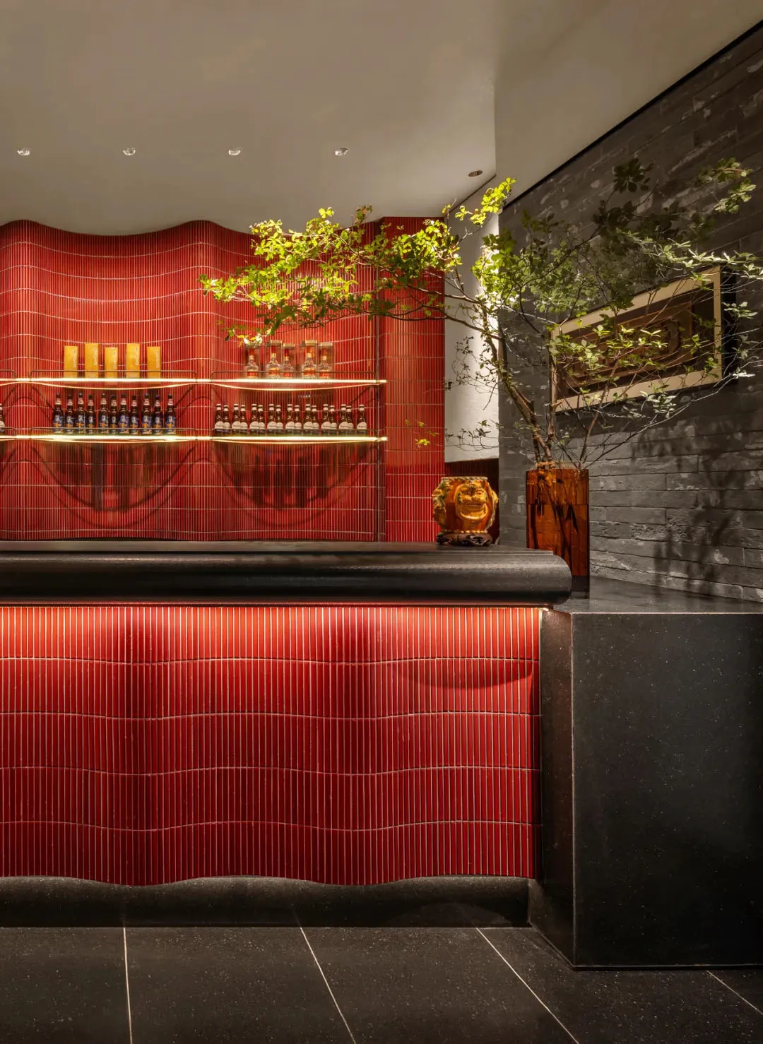 A cozy bar area with a red countertop, striped wall, and wine glasses, vases, and bottles arranged on the counter