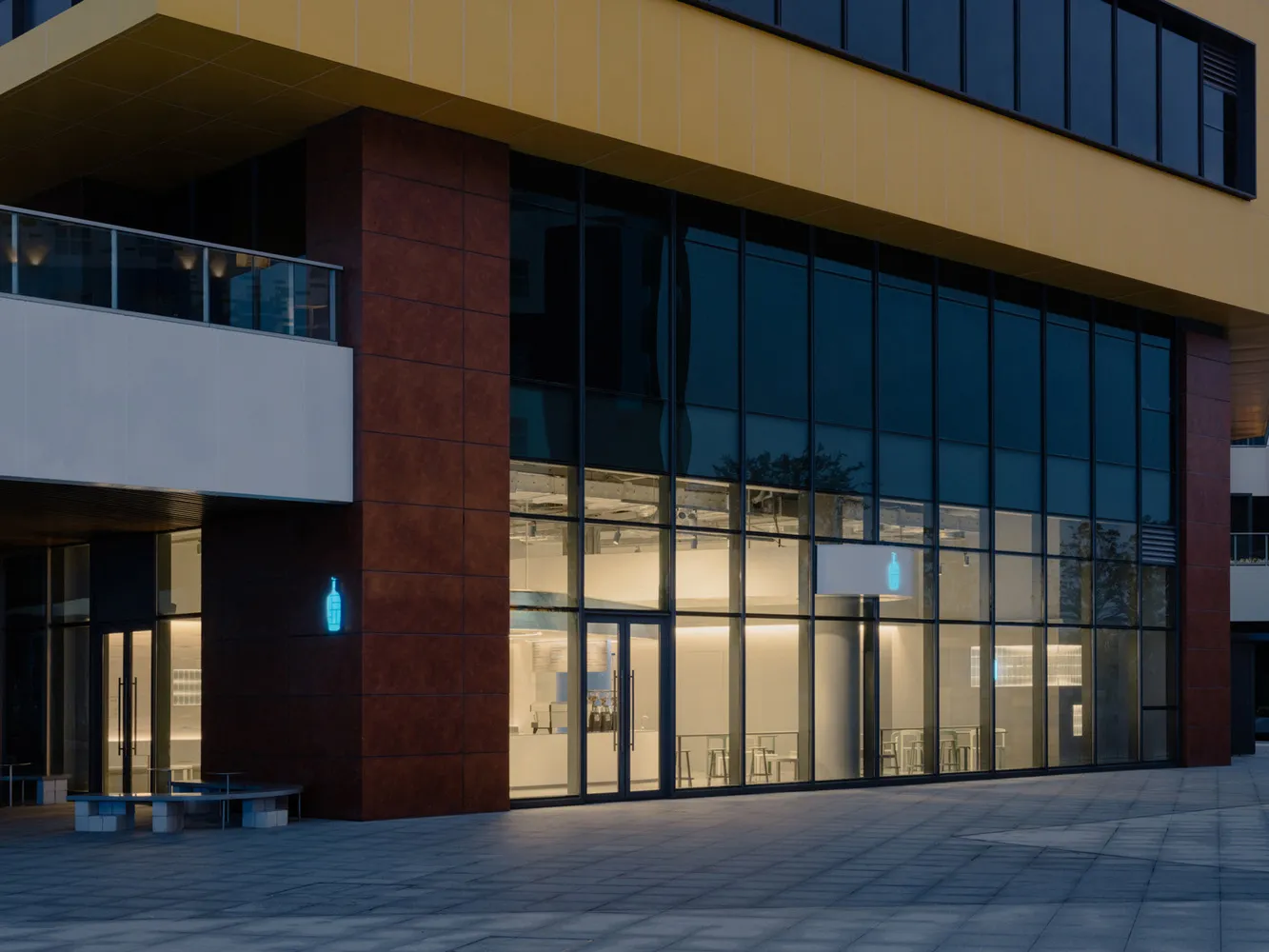 A modern building with a large glass window, featuring a combination of red brick and glass elements, set against a reflective surface