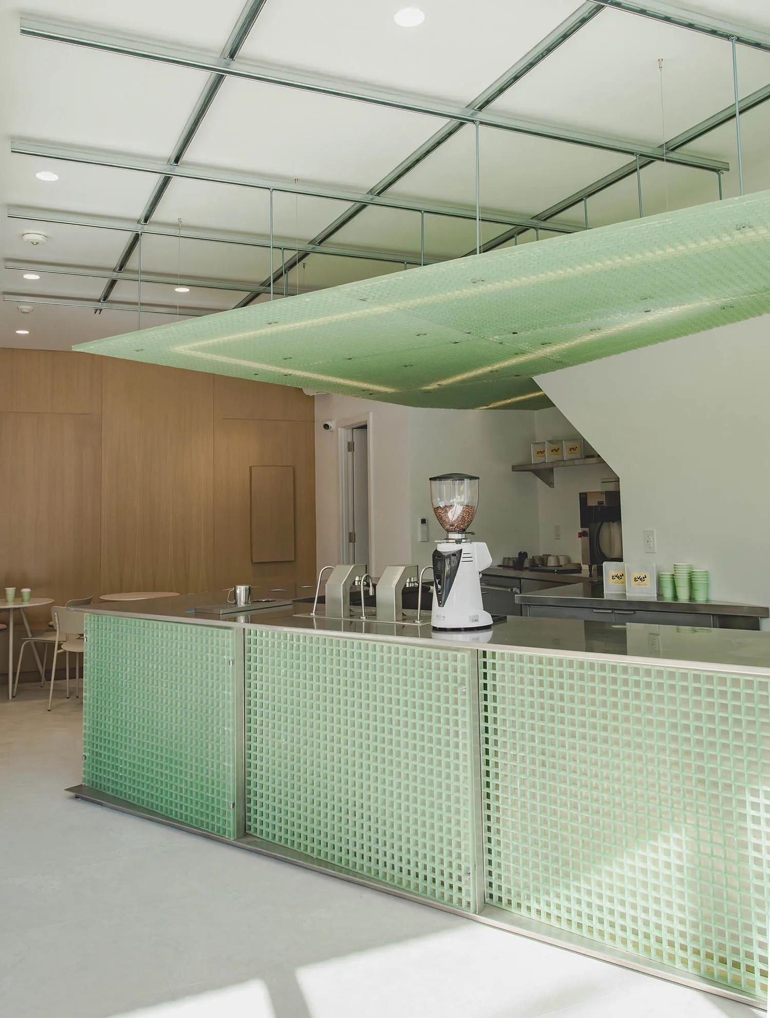 A modern kitchen with green walls, a countertop, chairs, a blender, cups, and bottles, creating a well-equipped and functional space