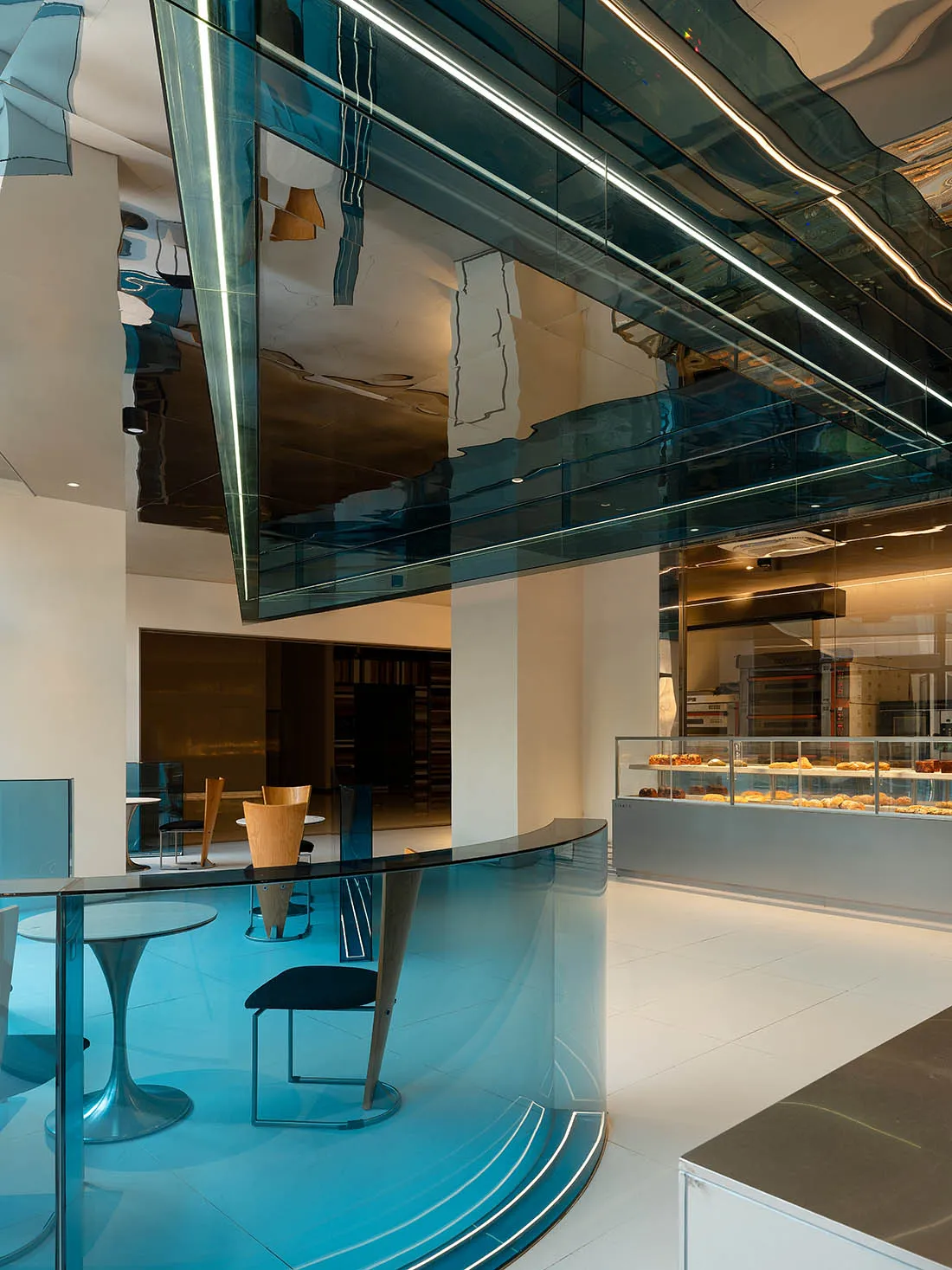 Modern restaurant interior with glass partition separating dining and kitchen areas, featuring tables, chairs, and a kitchen visible through the glass wall
