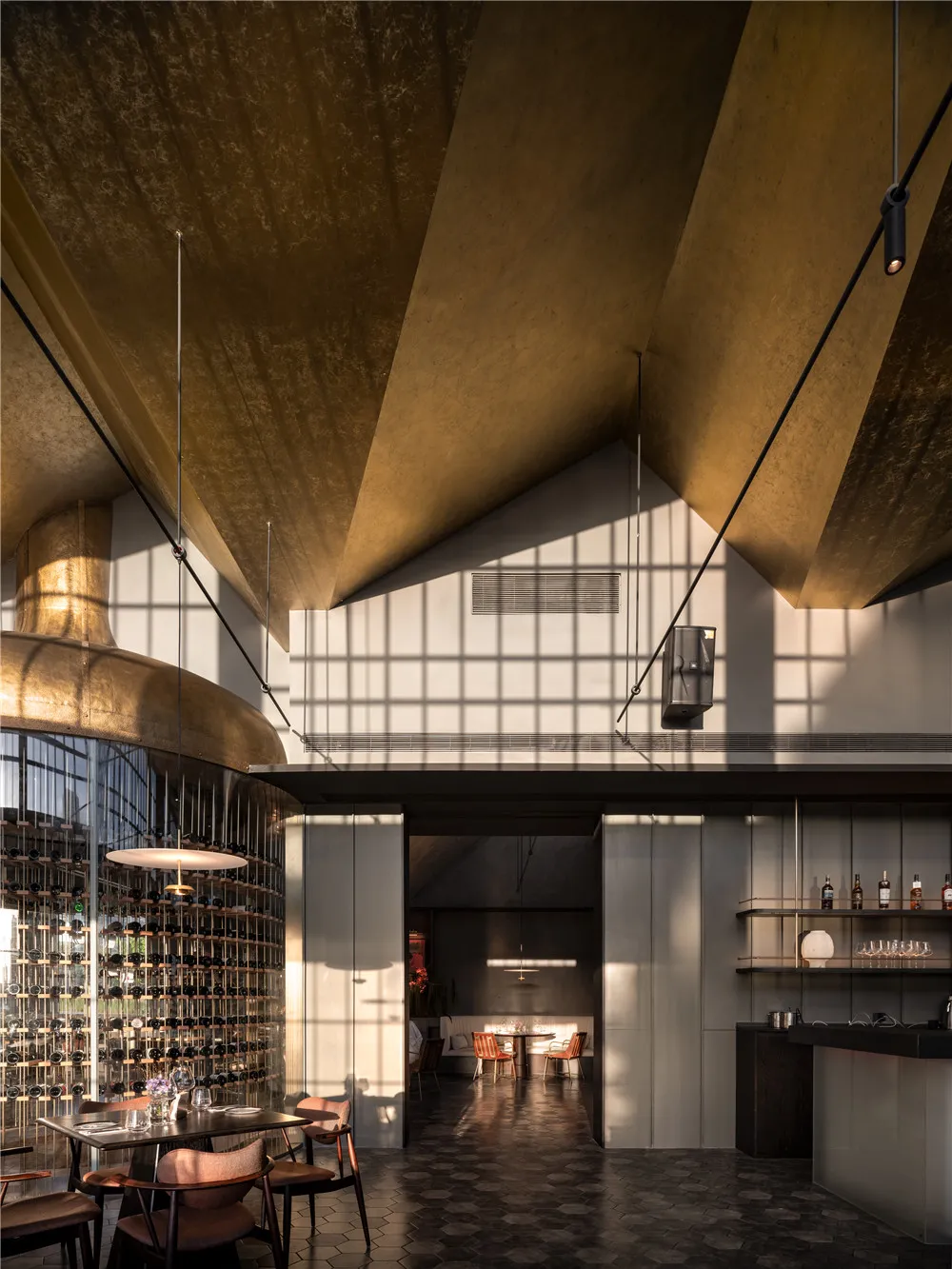 Modern bar area with gold ceiling and walls, wine glasses on countertops, and comfortable seating options