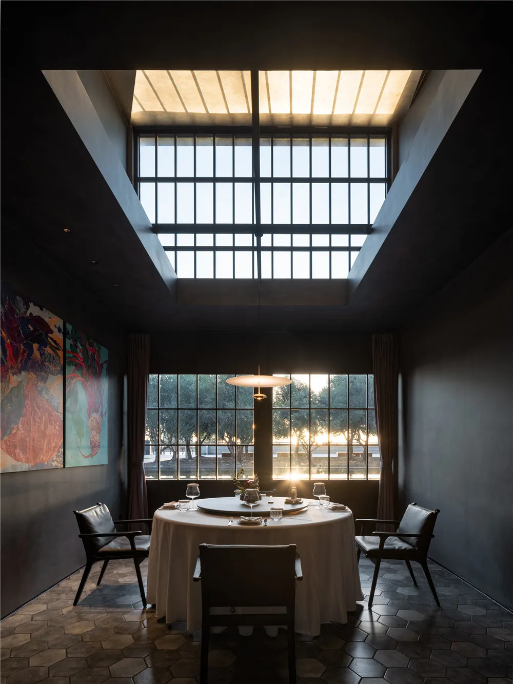 Dining area with two chairs around a round table, white tablecloth, and large window allowing sunlight to enter, creating a warm atmosphere