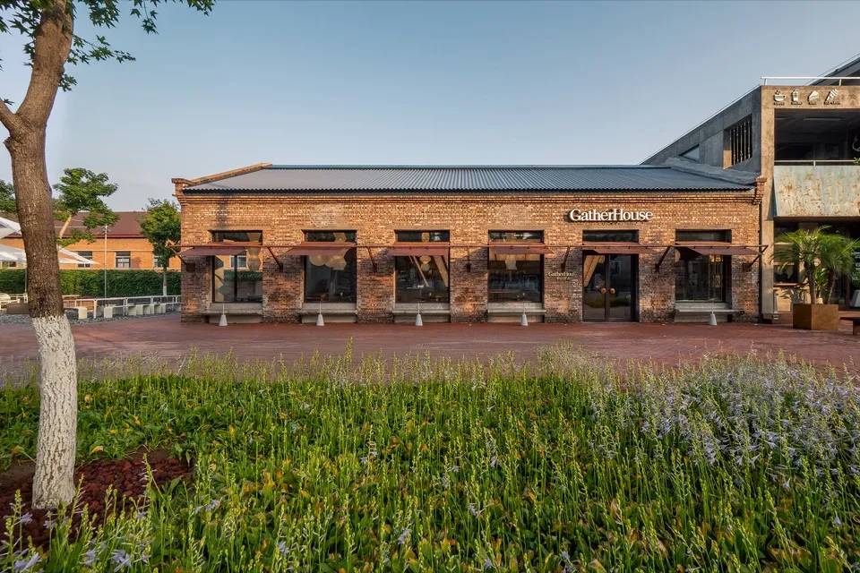 A brick building with a red roof and a large patio area with umbrellas, benches, and seating for guests