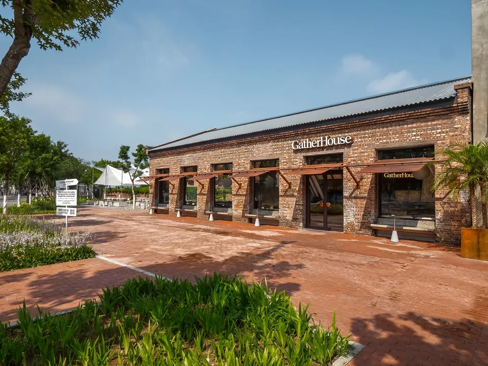 A rustic restaurant with a red roof and brick walls, featuring umbrellas and chairs outside, creating a warm and inviting atmosphere